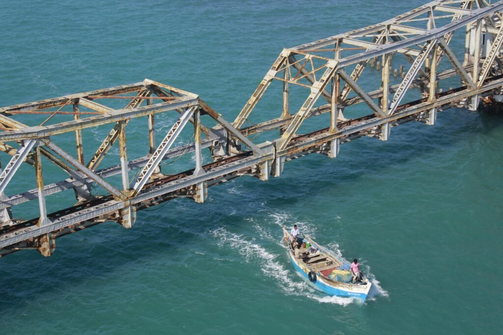 ROAM TAMIL NADU A fishing boat navigates beneath the historic rusty Pamban Bridge in clear blue waters.