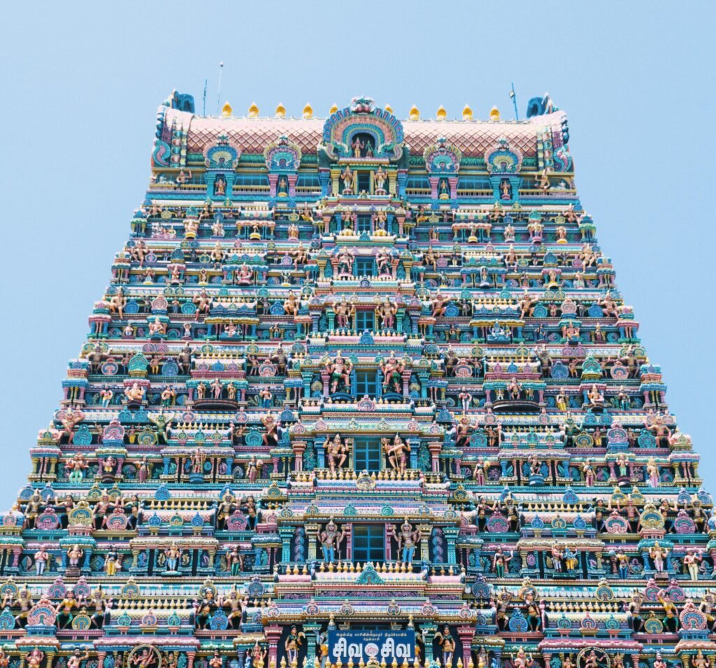 ROAM TAMIL NADU Intricately detailed Hindu temple tower with vibrant sculptures in a bright blue sky.